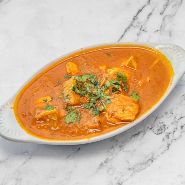 Chicken curry in a white oval dish, garnished with fresh cilantro, on a marble surface.