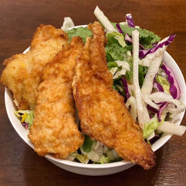 Crispy fried chicken pieces served in a white bowl with a fresh green and purple cabbage salad.