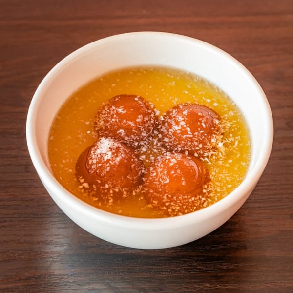 Four gulab jamun, Indian fried dough balls, in a white bowl with syrup and coconut flakes.