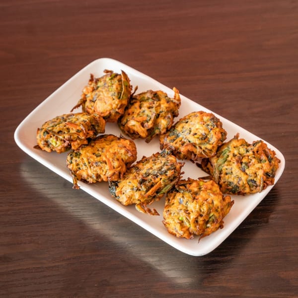 A white rectangular plate filled with golden-brown Indian pakoras on a dark wooden table.