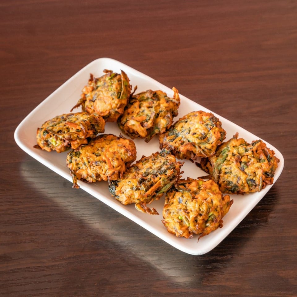 A white rectangular plate filled with golden-brown Indian pakoras on a dark wooden table.