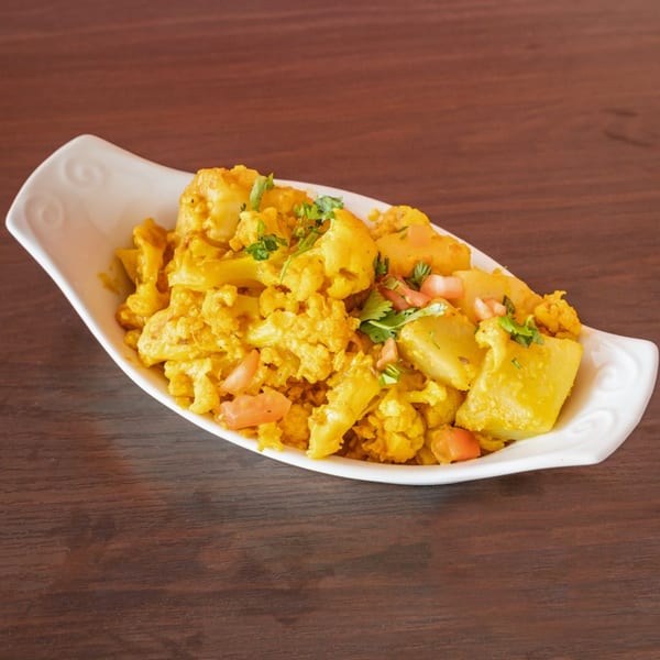 Aloo Gobi, an Indian dish with cauliflower and potatoes, garnished with cilantro and tomatoes.