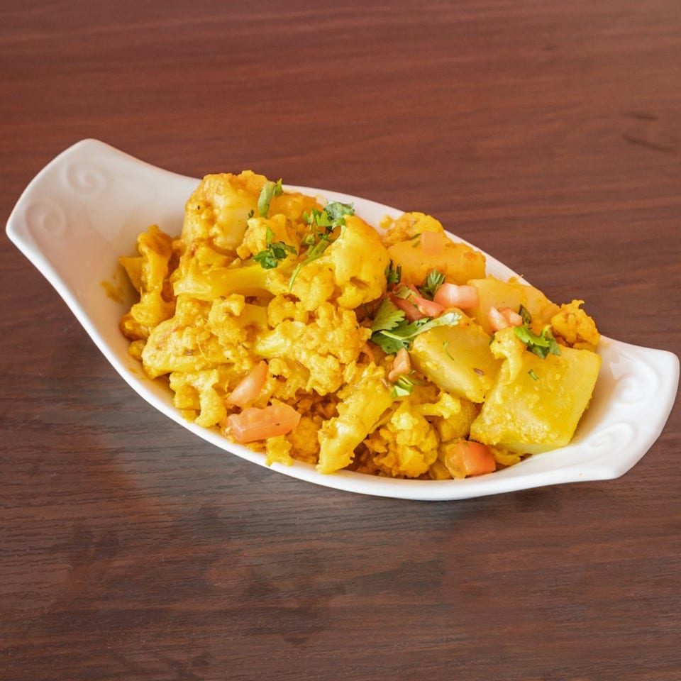 Aloo Gobi, an Indian dish with cauliflower and potatoes, garnished with cilantro and tomatoes.