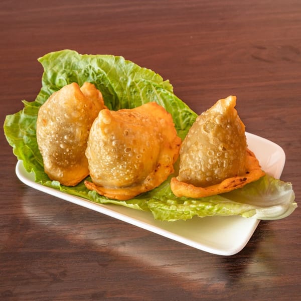 Three golden-brown samosas, an Indian appetizer, rest on a bed of fresh green lettuce leaves.