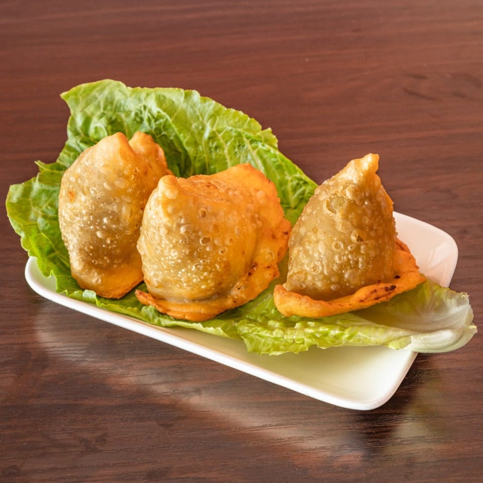 Three golden-brown samosas, an Indian appetizer, rest on a bed of fresh green lettuce leaves.