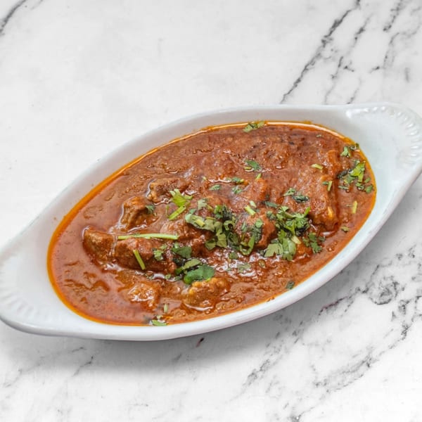 Rich Indian curry with meat pieces and fresh cilantro, served in a white oval dish.