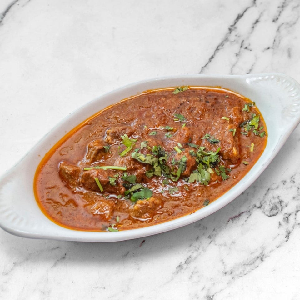 Rich Indian curry with meat pieces and fresh cilantro, served in a white oval dish.